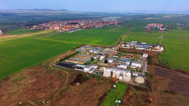 Wastewater treatment plant located in the countryside. Dense urban landscape of the little city at backdrop. Aerial view.