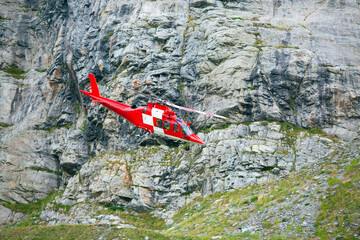 Red rescue helicopter flying along steep rocky mountain wall © AlexR