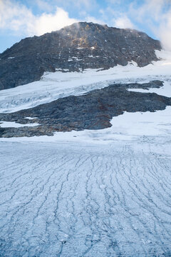 Melting alpine glacier with textured ice surface and rocky mountain
