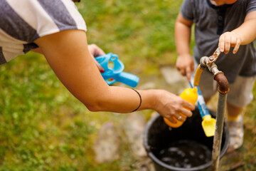 Mother and son filling toy gun with water while playing in the backyard of their home