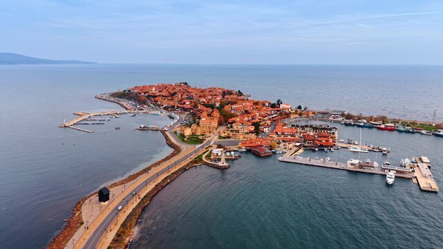 Cars go by the road along the dam leading to the peninsula. Red-roofed cityscape of modern Nessebar, Bulgaria.