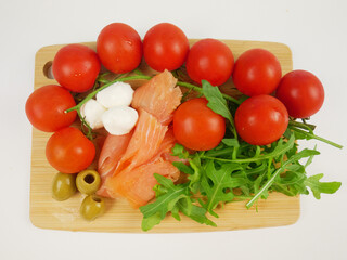 Closeup of smoked salmon with cherry tomatoes, arugula, olives and cheese on wooden board, healthy Mediterranean appetizer salad recipe for lunches and dinners, step-by-step