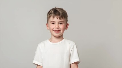 A young boy holding a slice of watermelon in front of a white background. The boy is wearing a white tshirt and has a cheerful expression.