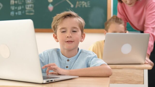 Caucasian boy working at laptop while diverse children programing software system. Teacher and student looking at boy laptop screen to solve problems and support coding engineering prompt. Pedagogy.