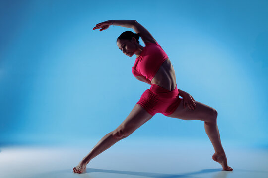 Woman performing reverse warrior side bend stretch in blue studio for mobility and posture