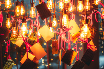 telephoto shot of glowing vintage filament bulbs with hanging greeting cards and pink ribbons, festive Christmas and New Year decoration, warm golden light, bokeh background, cozy holiday atmosphere