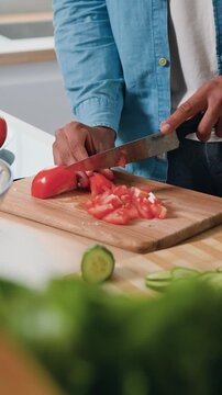 Close-up. Male hands cutting tomatoes with knife in kitchen while man is cooking salad from fresh raw vegetables. Healthy food concept. Slow motion.
