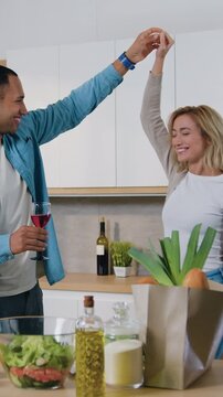 Man and woman clinking glass of wine and drink in cozy kitchen. Happy loving couple in love have romantic evening dancing in the kitchen. Slow motion.