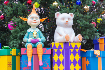 New Year's composition: a polar bear and an elf sit on gift boxes against the backdrop of a decorated Christmas tree.