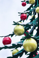 A green metal Christmas tree with large yellow and red balls. Part of the frame.