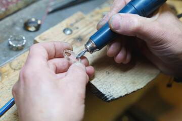 Jeweler using a rotary tool to polish a silver ring at a wooden workbench.