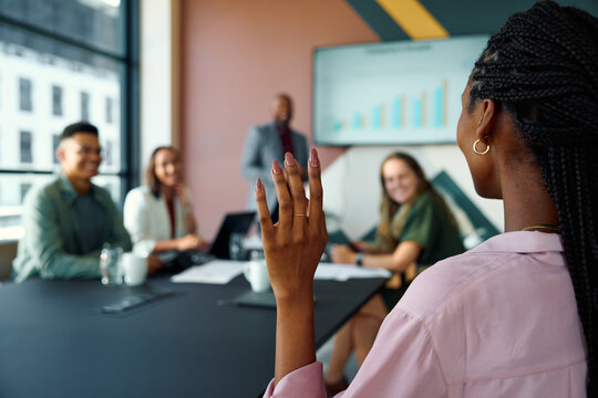 Confident businesswoman raising hand while discussing ideas with diverse team in boardroom during daytime - Powered by Adobe