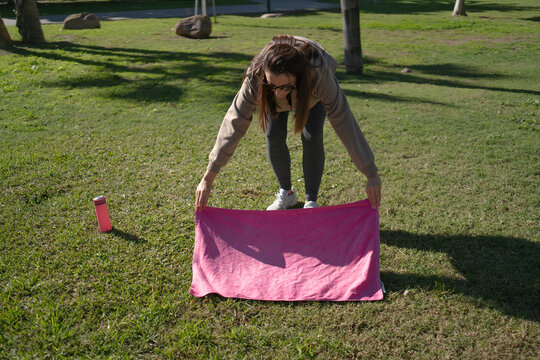 Woman spreading pink yoga mat on green grass