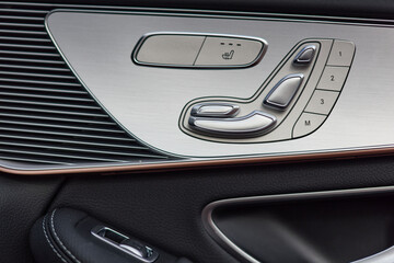 The car interior shows seat adjustment controls on the door panel, including seat heating, memory settings, and adjustable controls. Interior details also feature dark leather.