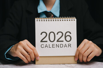 2026 calendar held by person in business suit on marble table, planning and organization concept with clear focus on year