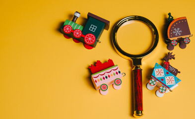 Christmas concept. Wooden toy train with magnifying glass on yellow background, colorful festive design and playful holiday spirit