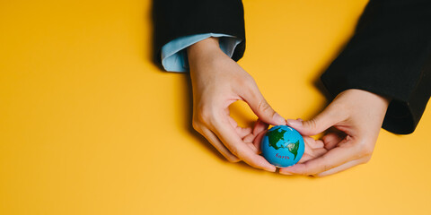 Love planet concept. Small globe held by hands on yellow background symbolizing care and protection of planet with warm and hopeful feeling