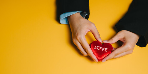 Red heart with love text held by hands on yellow background expressing affection and care in warm setting