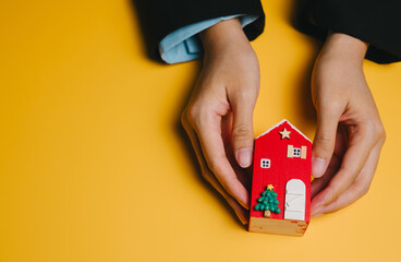 Christmas concept. Miniature house Hands Red Yellow background Christmas tree Star Door Human hand Decoration Small object Model Home Holding Wooden Toy Person Close