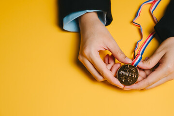 Winner concept. Gold medal winner medal hands holding medal achievement award victory celebration success symbol yellow background close up person holding medal
