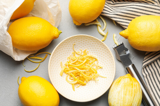 Fresh lemons with zest and zester tool on grey table, flat lay