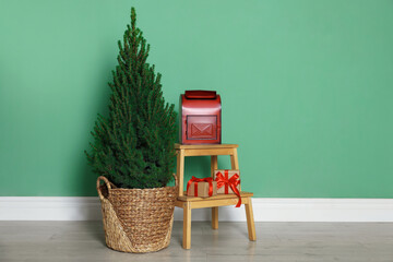 Potted small spruce tree, Santa's mailbox and gifts near green wall indoors, space for text. Christmas decor