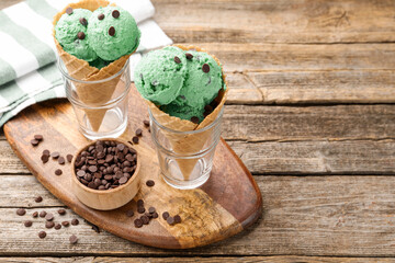 Tasty mint chocolate chip ice cream in waffle cones on wooden table. Space for text