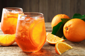 Glasses of refreshing spritzer cocktail and oranges on wooden table, closeup