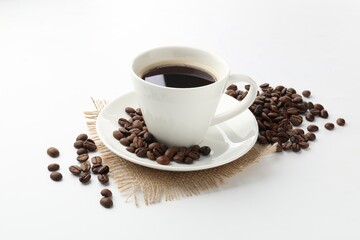 Cup of aromatic coffee and roasted beans on white background