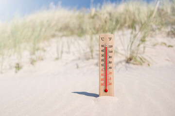 Wooden celsius and fahrenheit scale thermometer in the sand. Ambient temperature plus 50 degrees. Hot summer day