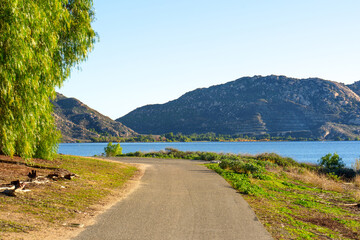 Sunlit Lakeside Path With Distant Rocky Mountains
