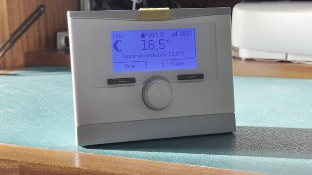 Close-up of digital room thermostat with blue backlit LCD in french, indoor home heating control, temperature regulation and energy-saving smart HVAC concept