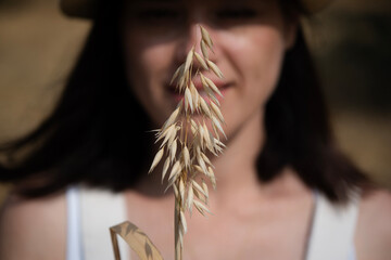 Young woman on a farm holding a ripe oat plant close to her face, a symbol of natural harvest, organic farming, and sustainable agriculture in a rural field setting