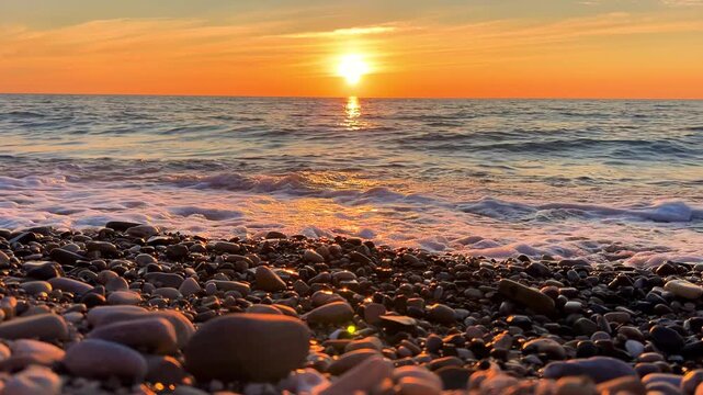 Orange sunset in Tuapse, sea waves with foam run to the shore. The Black Sea coast at sunset in the clouds. Pebble beach in the village of Agoy. The stormy sea in the evening. 4К