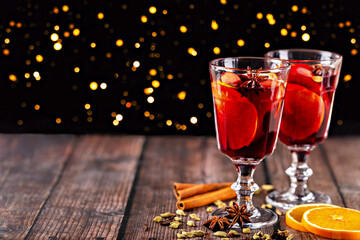 Mulled wine. Refreshing beverage served in elegant glasses, featuring apple slices and spices, placed on rustic wooden table with blurred sparkling background, creating warm and inviting atmosphere