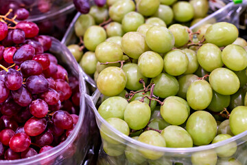 Organic market. Fresh green and red grapes are beautifully arranged in clear containers, showcasing their vibrant colors and textures, creating an inviting atmosphere in lively market environment