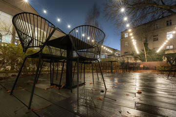 Zamknięty ogródek restauracyjny z zapalonymi lampkami i metalowymi krzesłami