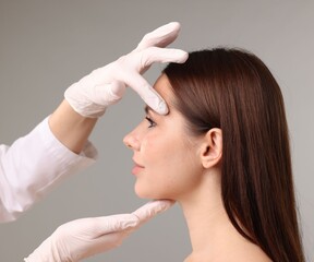 Fototapeta premium Doctor checking patient's face before plastic surgery operation on grey background, closeup