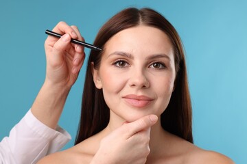 Obraz premium Doctor drawing marks on patient's face for plastic surgery operation against light blue background, closeup