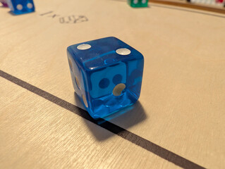 Close-up of blue transparent die on wooden board of tabletop game. Gaming, leisure, hobby, dexterity, strategy, skill, entertainment, indoor activity, competition, play, scoring, luck, rolling, pips.
