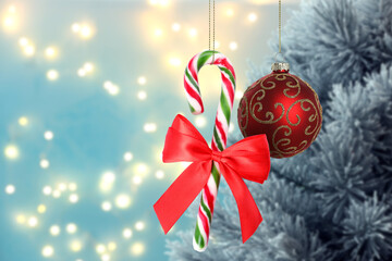 Beautiful Christmas ornament and candy cane hanging against blurred tree. Winter holidays greeting card
