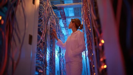 Data Center Technician: A focused technician meticulously examines the intricate web of data cables within a modern server room, illuminated by cool blue lights. - Powered by Adobe