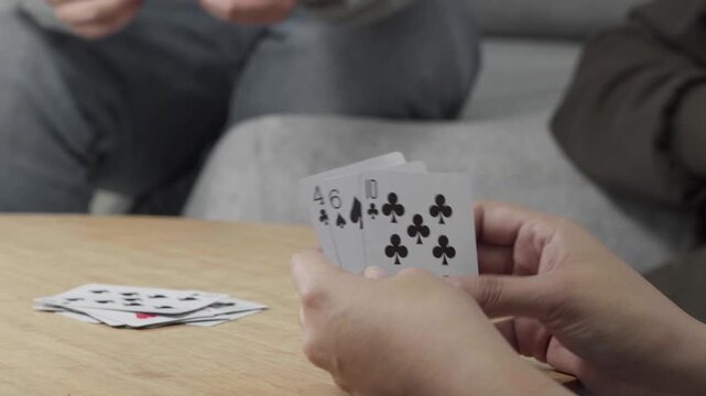 Two people playing cards at a table at home, focusing on their hands and cards during a casual and social card game.