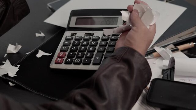 Man sitting at an office desk destroying bills and financial documents, expressing intense stress and anger caused by debt, surrounded by work tools and paperwork.
