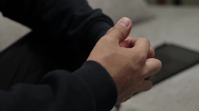 Close-up of a man sitting while nervously moving his thumbs in circular motions, hands intertwined, expressing worry and inner tension.
