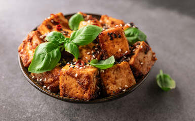 Fried tofu with sesame seeds, soy sauce, spices decorated with fresh basil leaves on gray concrete table top view. Healthy Asian food concept. Vegan food.