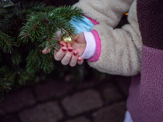 Child's hands with red nail polish touching a golden Christmas bauble 