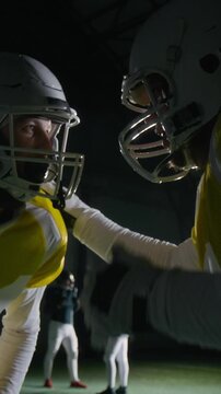 Medium vertical of two Caucasian male American or Canadian football players in protective helmets and yellow jerseys planning attack on rival end zone then hugging during match interval