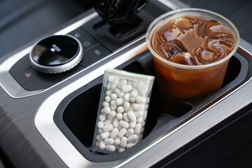 Close-up of a modern car interior with an iced coffee in a plastic cup and a container of white...