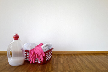 Red basket with white bath towels, pink rubber gloves, and a washing detergent bottle near the wall. Housekeeping, laundry, and home cleaning concept.